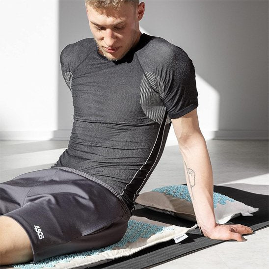 homme assis sur un tapis acupression gris et bleu